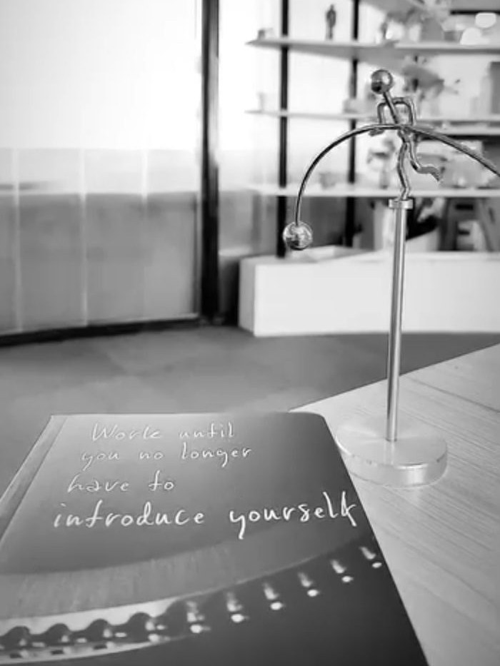 My desk: a notebook that reads 'Work until you no longer have to introduce yourself', beside a balancing figure